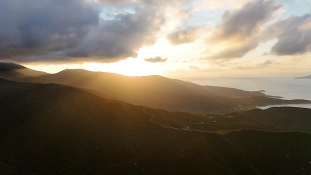 A breathtaking aerial view of sunrise over Erdek, Türkiye, featuring rolling hills and wind turbines.
