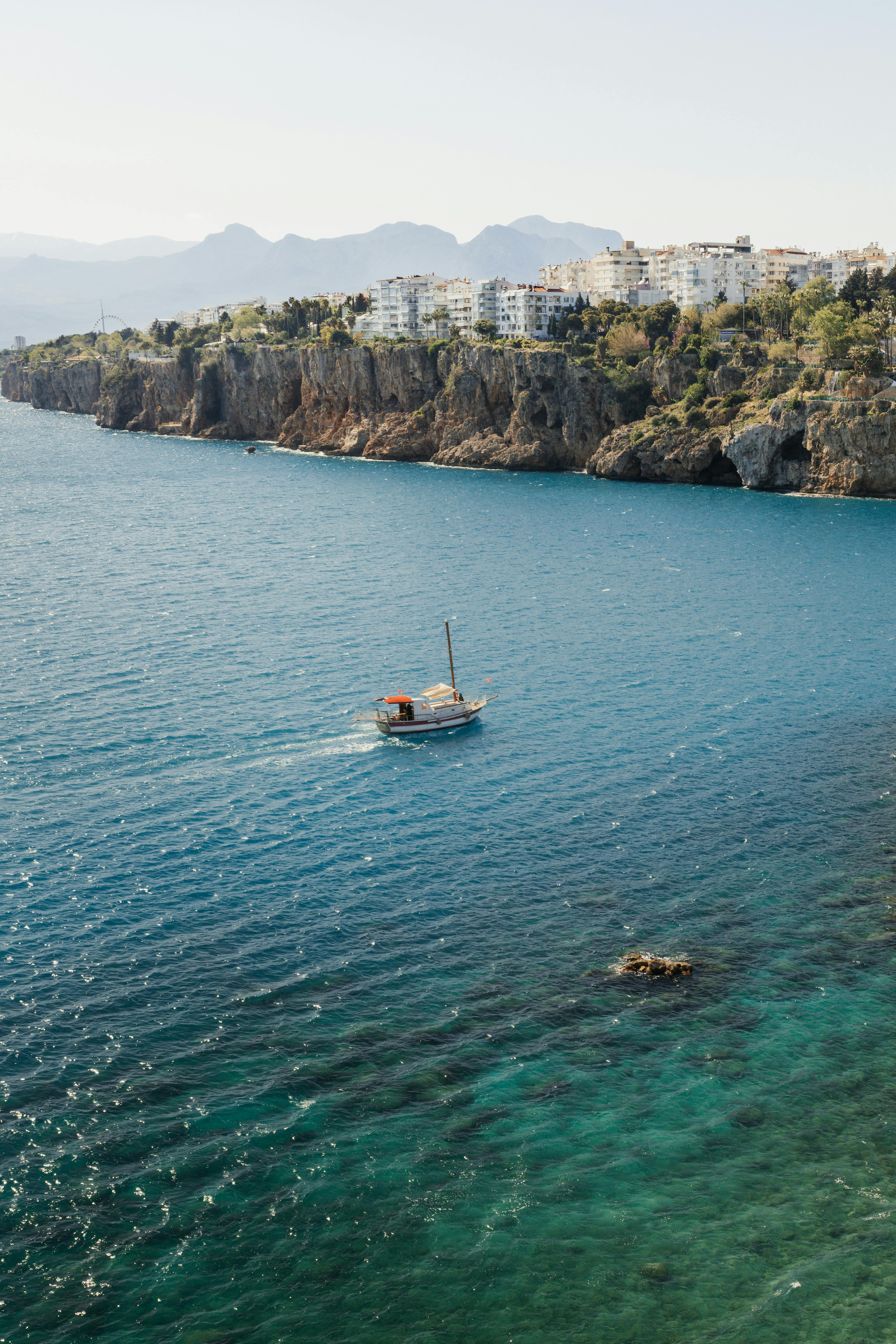 Picturesque Antalya coastline with a sailboat on the Mediterranean Sea under a sunny sky.