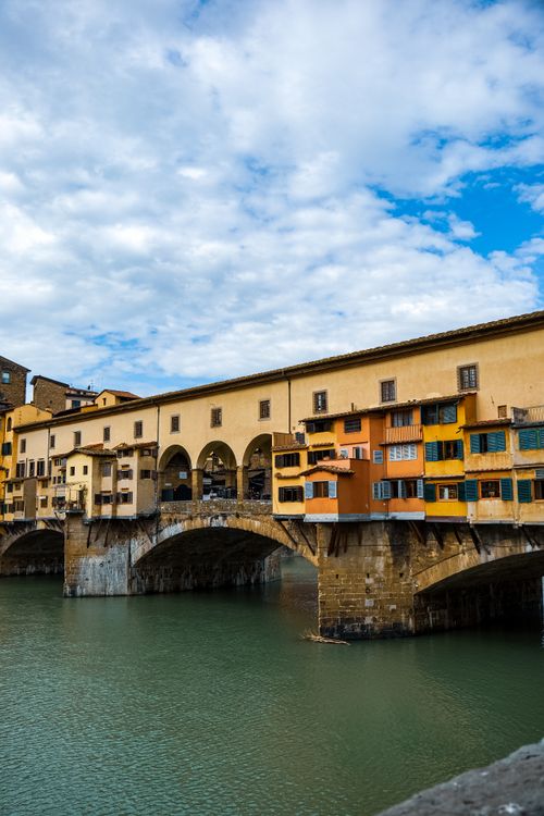 Free Iconic Ponte Vecchio Bridge over the Arno River in Florence, Italy under a partly cloudy sky. Stock Photo