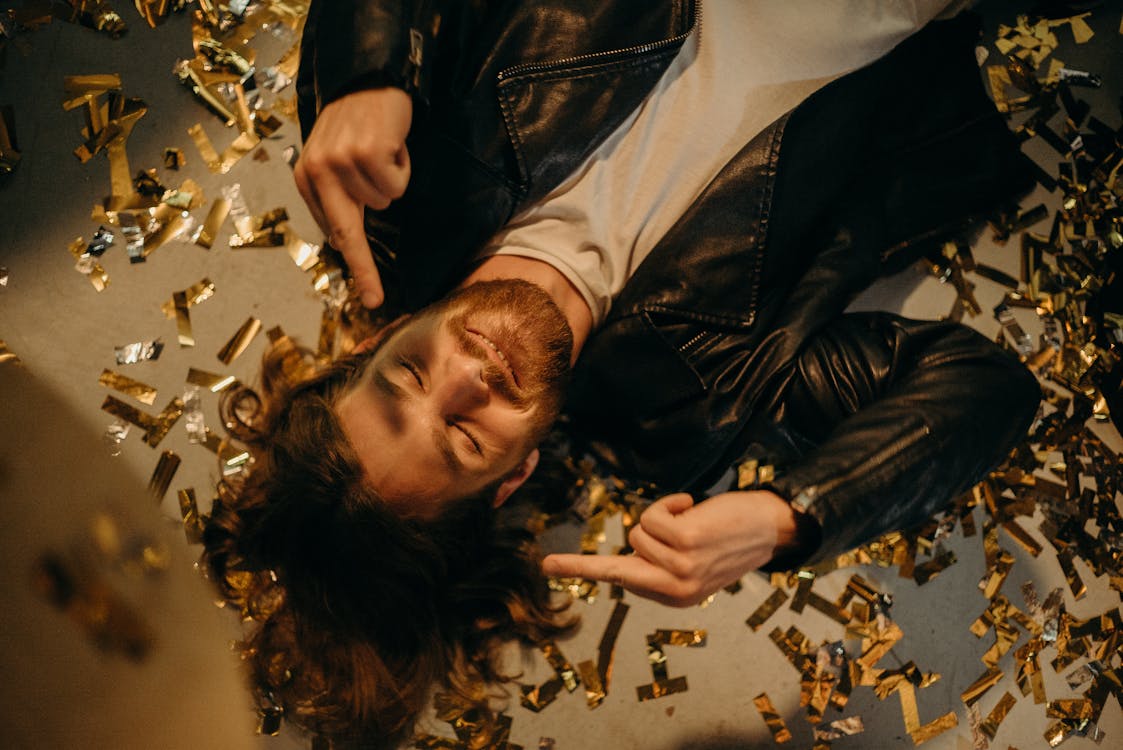 Man in Black Leather Jacket Lying On Floor Covered in Confetti