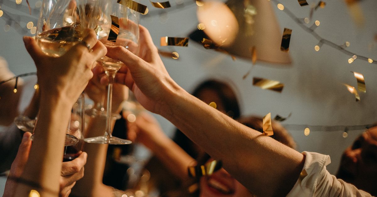 Hands raising champagne glasses in a toast with gold confetti falling