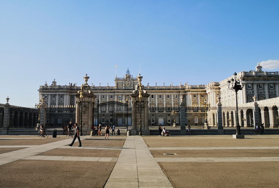 Impresionante vista del Palacio Real de Madrid con gente paseando bajo un cielo azul claro.