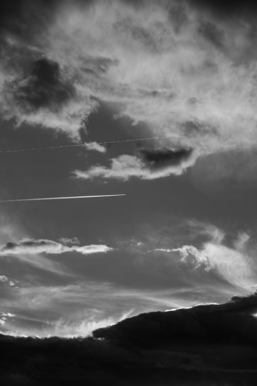 Free Black and white image of a dramatic sky with clouds and contrails during dusk. Stock Photo