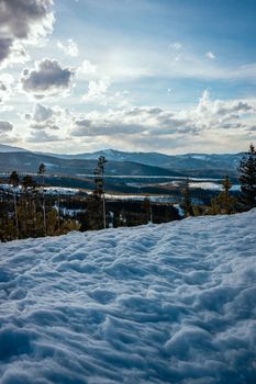 Peaceful winter landscape with snow and mountains under a cloudy sky.