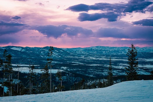 Captivating view of a winter sunset over snow-covered mountains and forest with dramatic clouds.