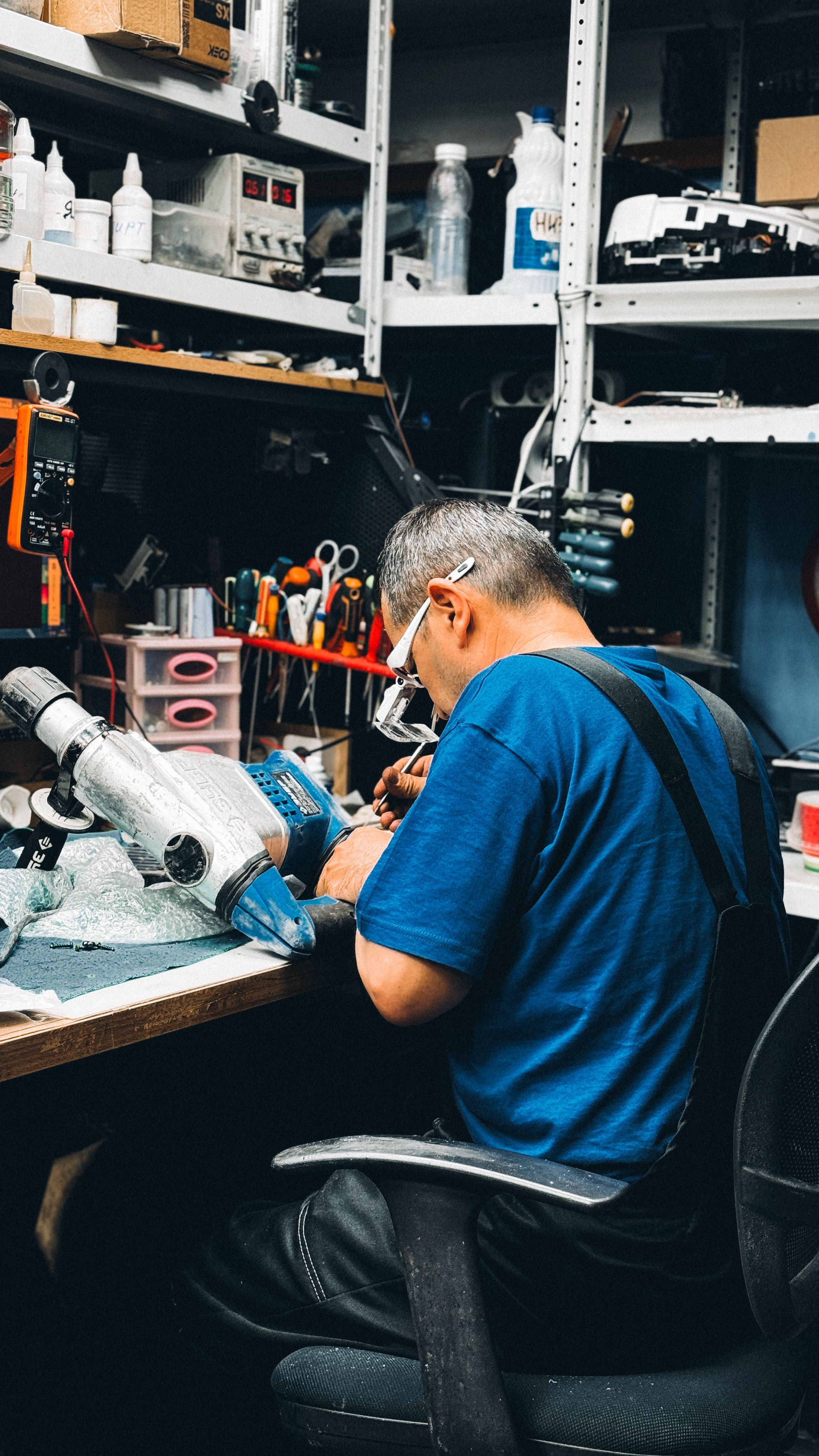 Skilled technician working on electronic devices in a cluttered workshop, showcasing precision and concentration.