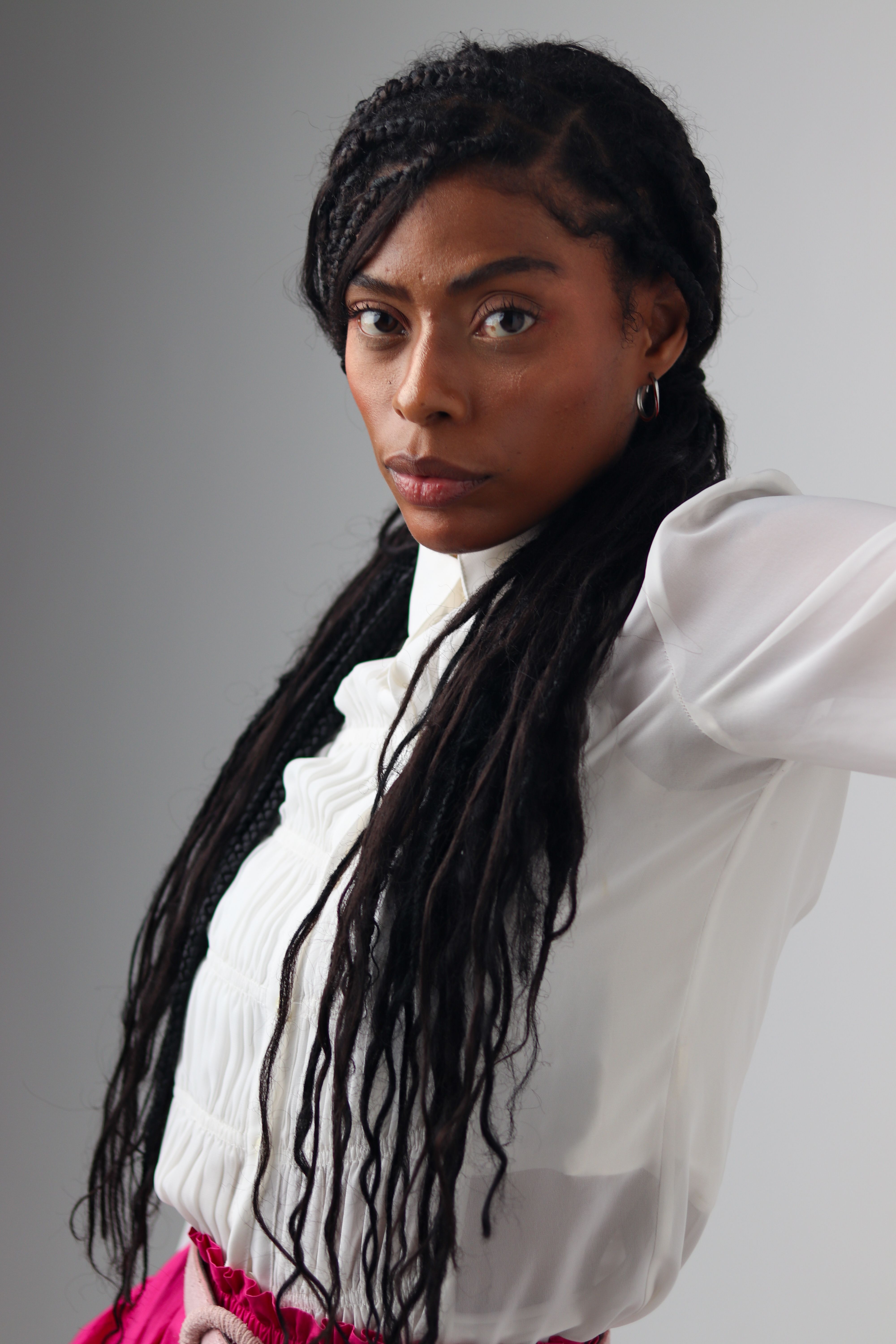 Portrait of a confident woman with long braids in a white shirt, posing in a studio setting.