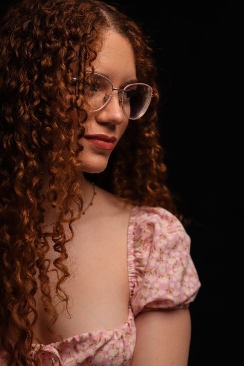 Free Beautiful woman with curly hair and glasses wearing a floral top against a dark background. Stock Photo