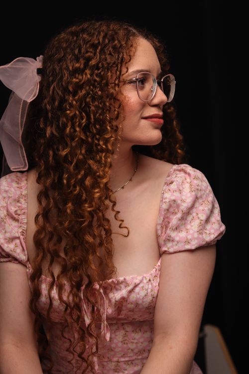 Free Charming portrait of a woman with curly hair, wearing a pink floral dress with glasses and a bow. Stock Photo