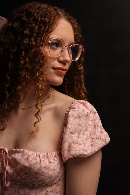 Free Elegant portrait of a young woman with curly hair and glasses, wearing a floral pink dress. Stock Photo