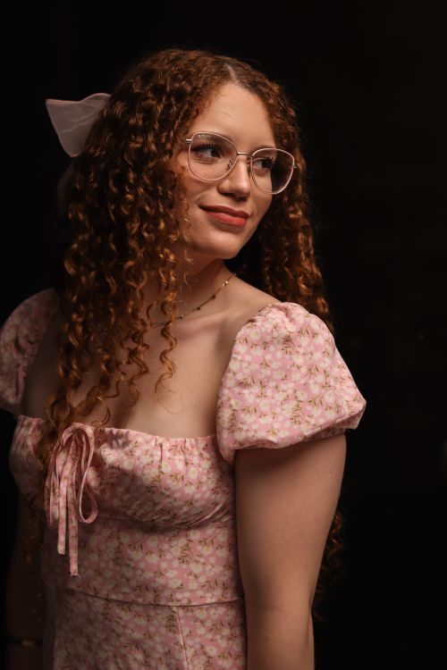 Free A beautiful woman with curly hair and glasses wearing a pink floral dress, looking to the side with a serene expression. Stock Photo