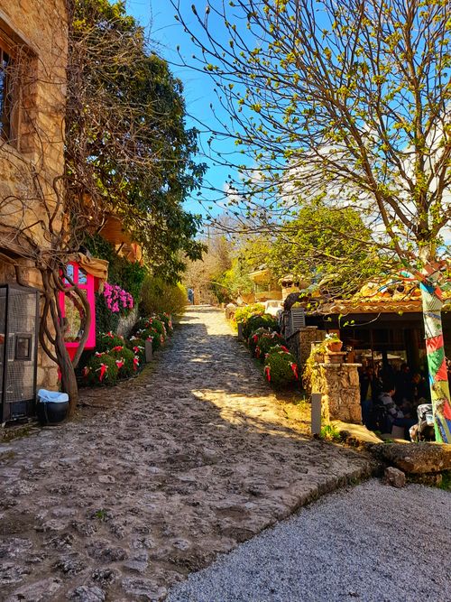 Free Picturesque cobblestone path lined with colorful flowers and rustic stone buildings on a sunny day. Stock Photo