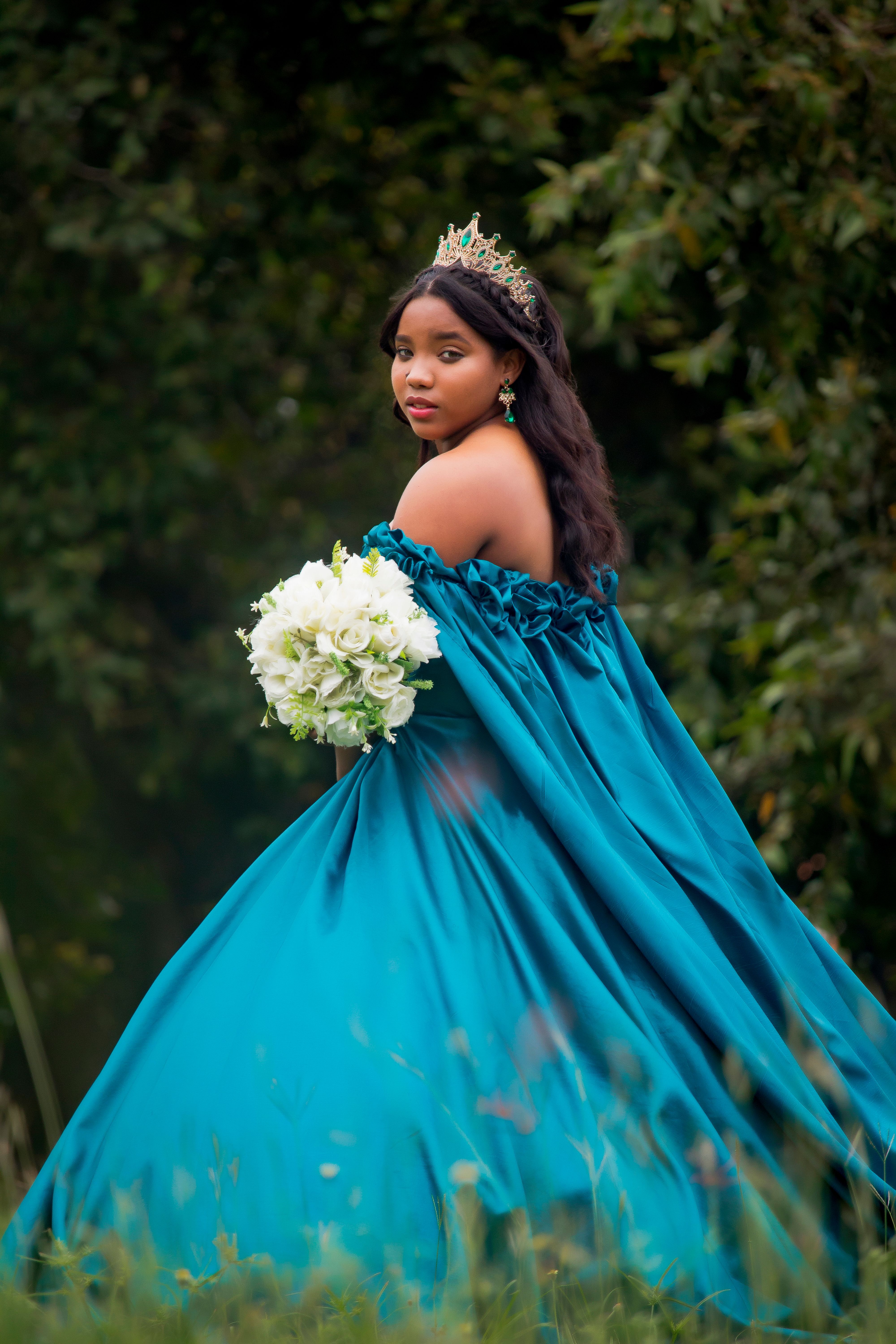 Stunning quinceañera portrait in a flowing teal gown with a lush green backdrop, Puerto Plata.