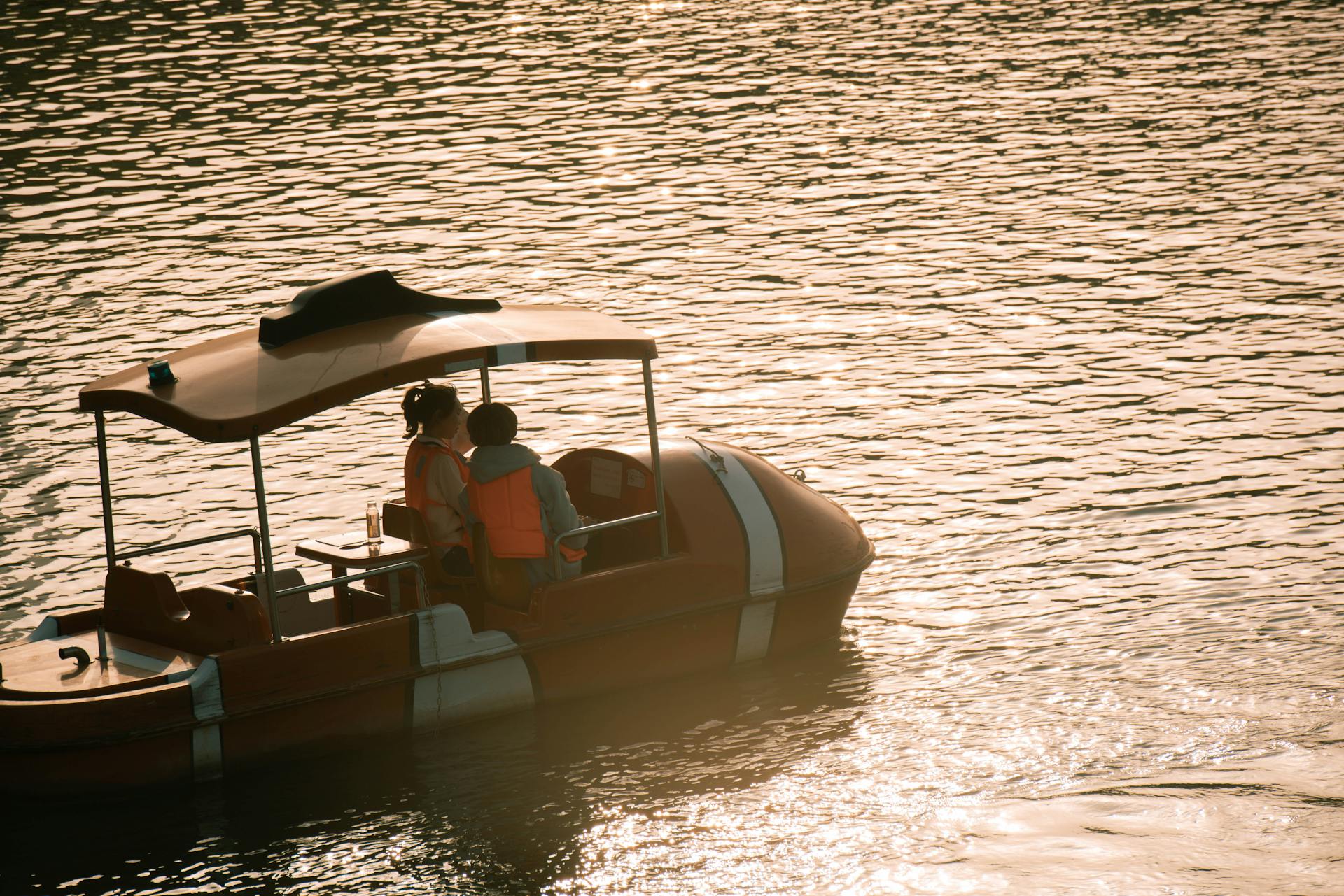 Two people enjoy a peaceful boat ride at sunset on a shimmering body of water.