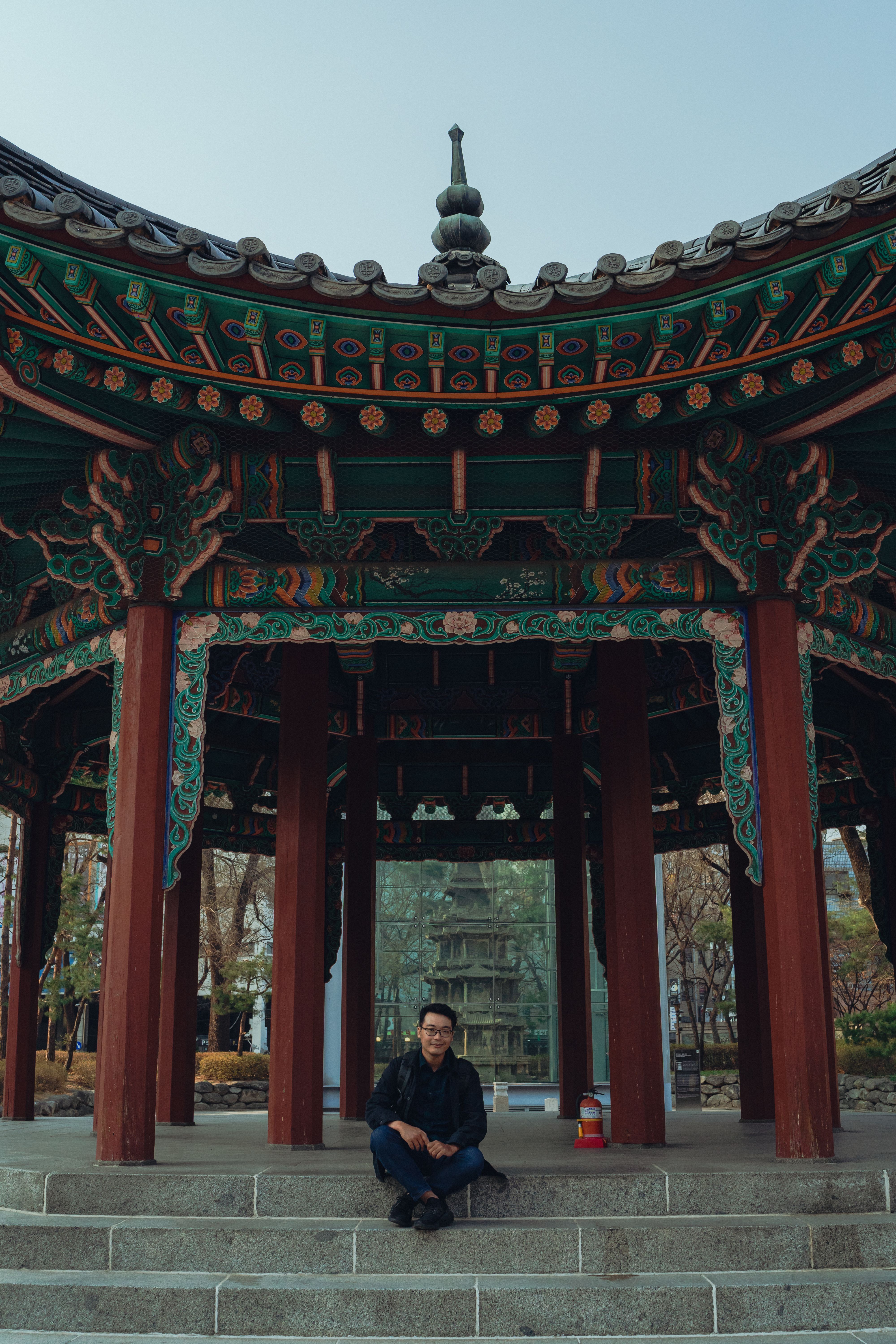 A man sits in a traditional Korean pavilion in Seoul, showcasing intricate architecture.