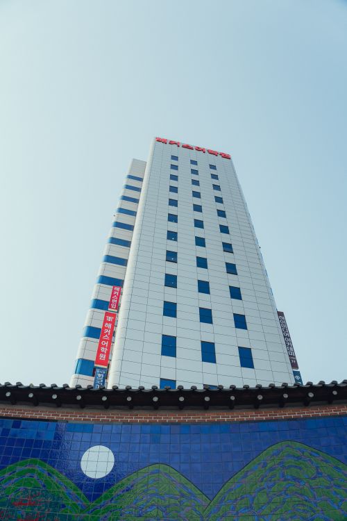 Free Tall white skyscraper with Korean text, behind a traditional wall with blue tiles and moon motif in Seoul. Stock Photo