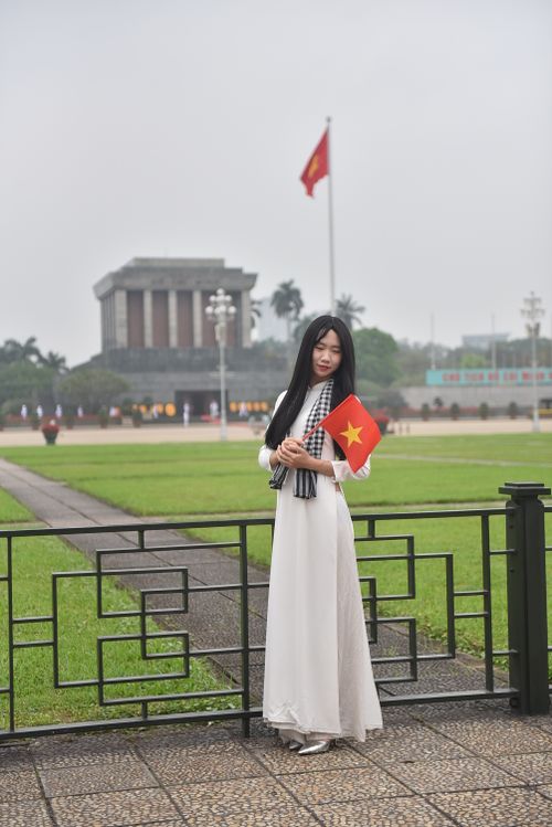 Free A young woman in traditional attire holding a Vietnamese flag at a historic site. Stock Photo