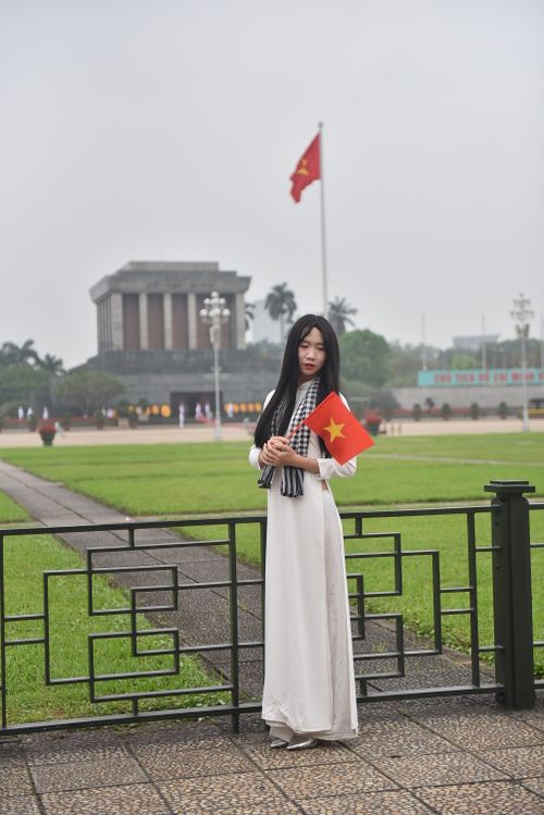 Free Young woman in traditional dress holding Vietnamese flag at Ho Chi Minh Mausoleum, Hanoi. Stock Photo