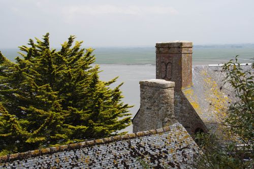 Free View of Mont Saint-Michel's rooftop and lush surroundings, capturing timeless architecture and coastal beauty. Stock Photo