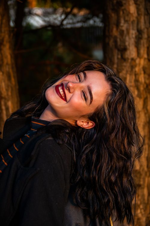 Free Smiling woman posing outdoors with vibrant makeup and natural surroundings. Stock Photo