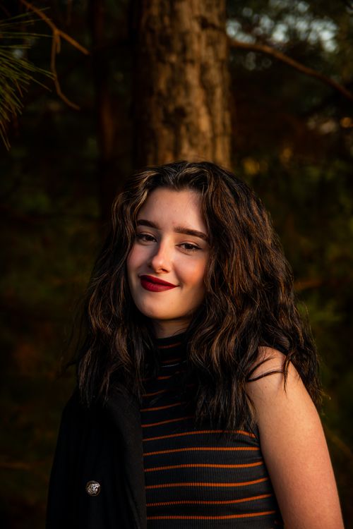 Free A young woman with curly hair smiling in a forest. Natural light enhances the ambiance. Stock Photo