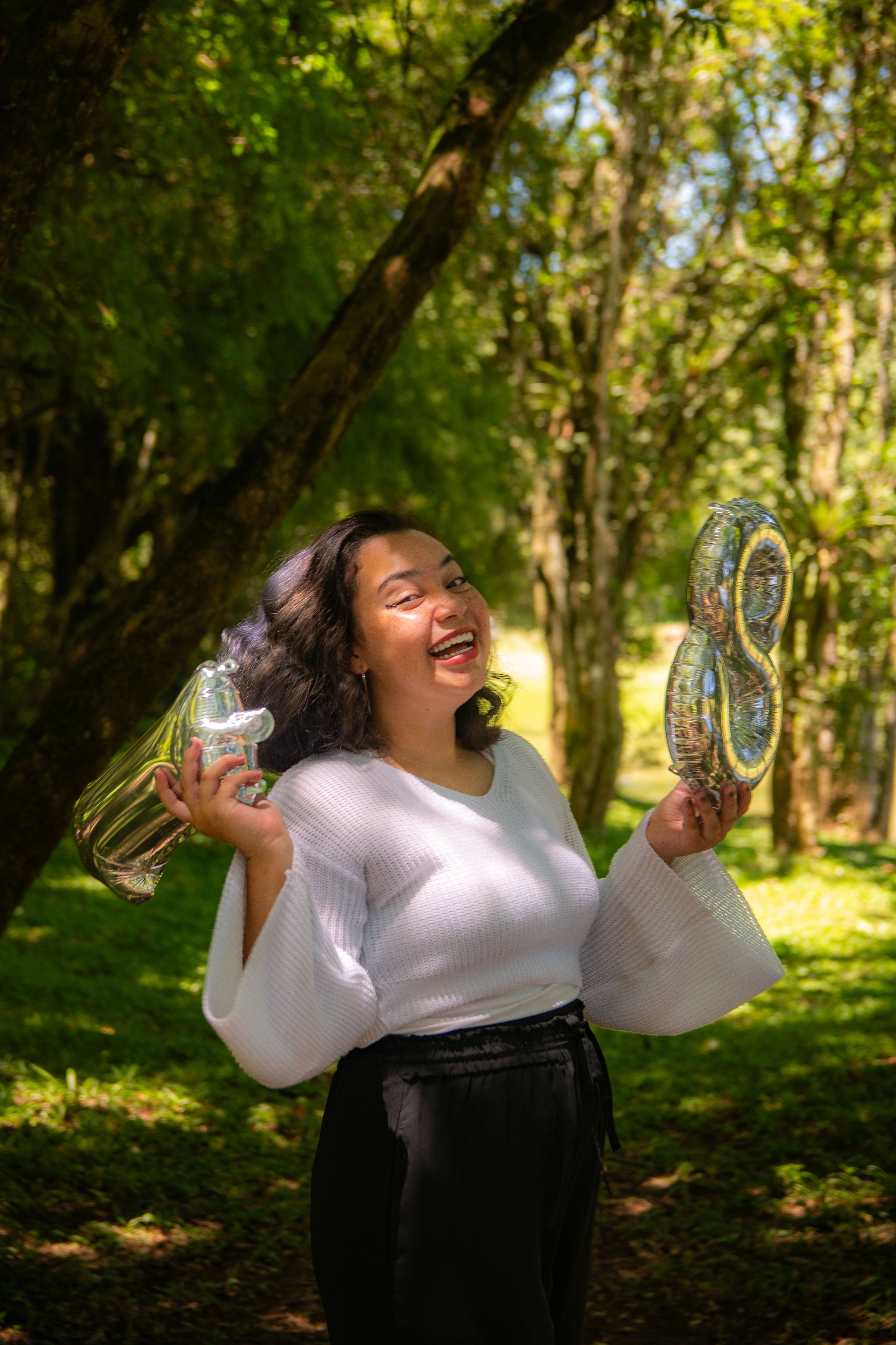Smiling woman holding balloons in forest, celebrating birthday outdoors.