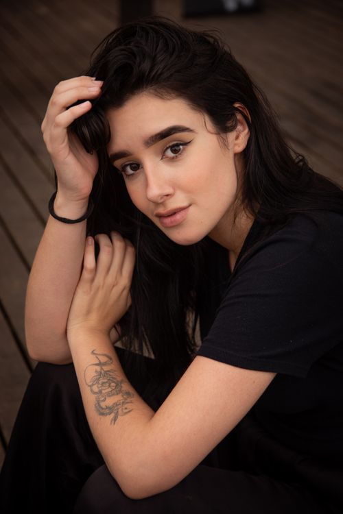 Free Striking portrait of a young woman with tattoo, sitting outdoors on wooden deck. Stock Photo