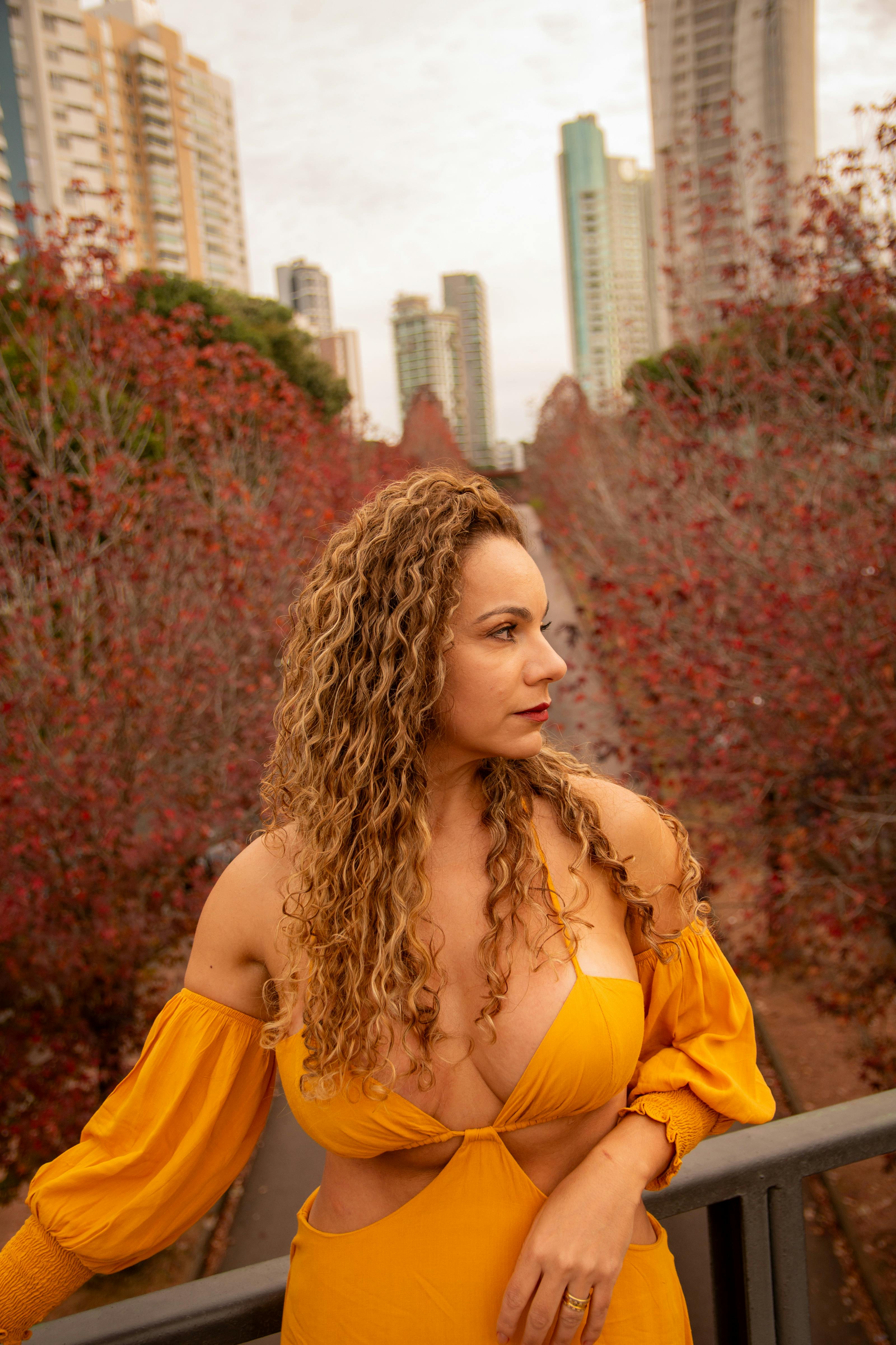 Stylish woman in a vibrant yellow dress standing on a bridge with city skyline backdrop.