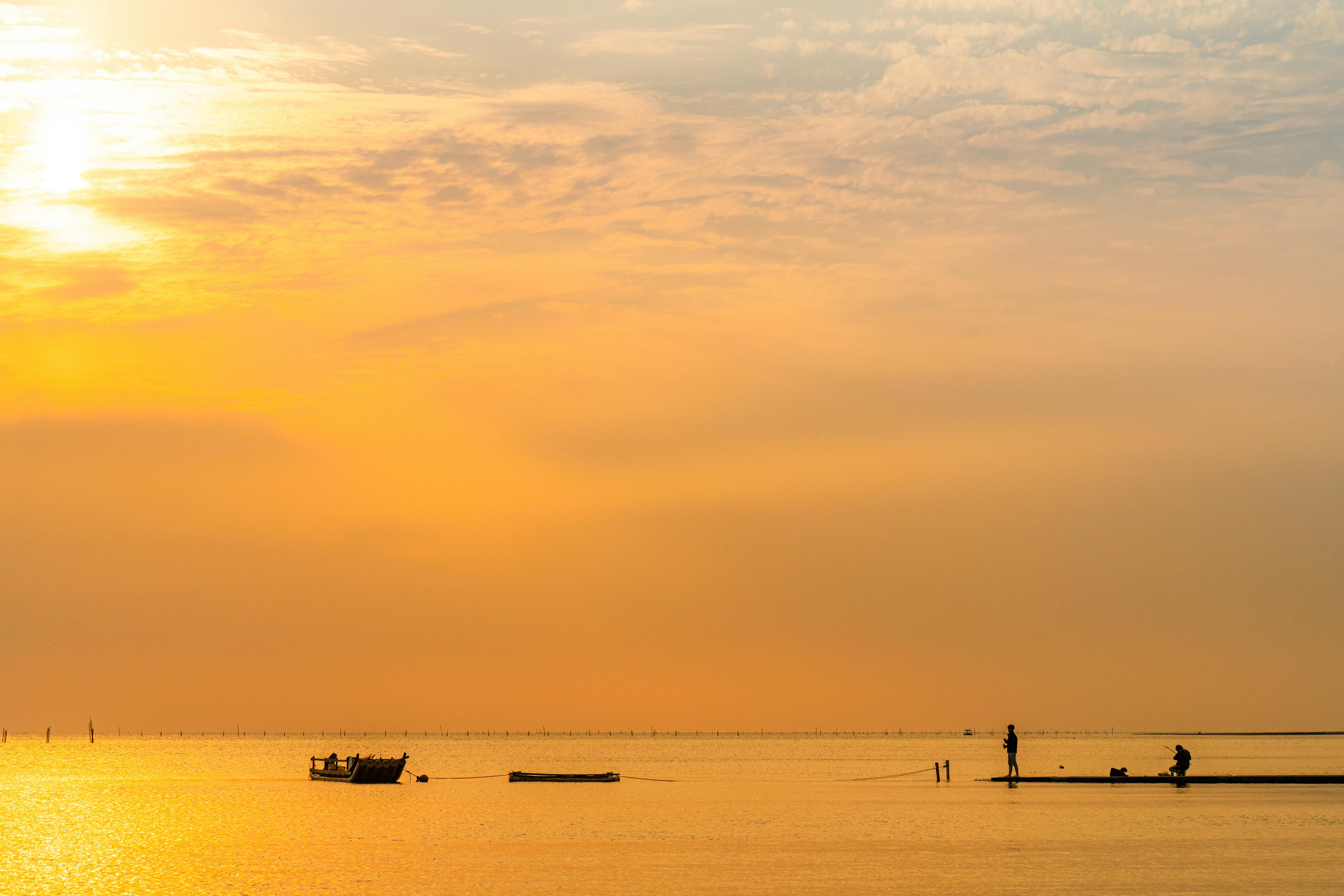 Serene sunset over Taiwan's beach with silhouettes of people and boats