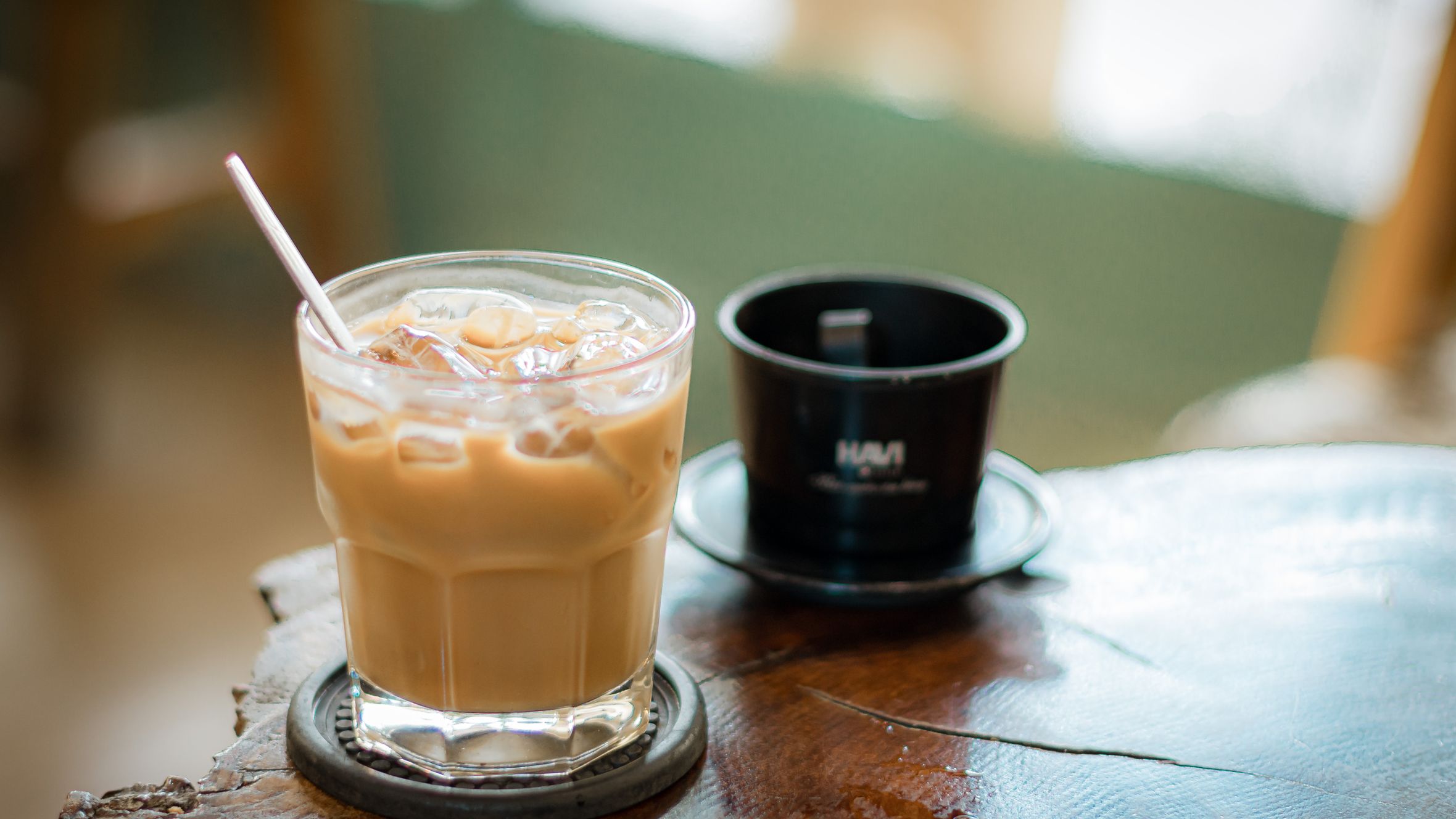 Glass of iced coffee and phin filter on rustic table in cozy cafe setting.