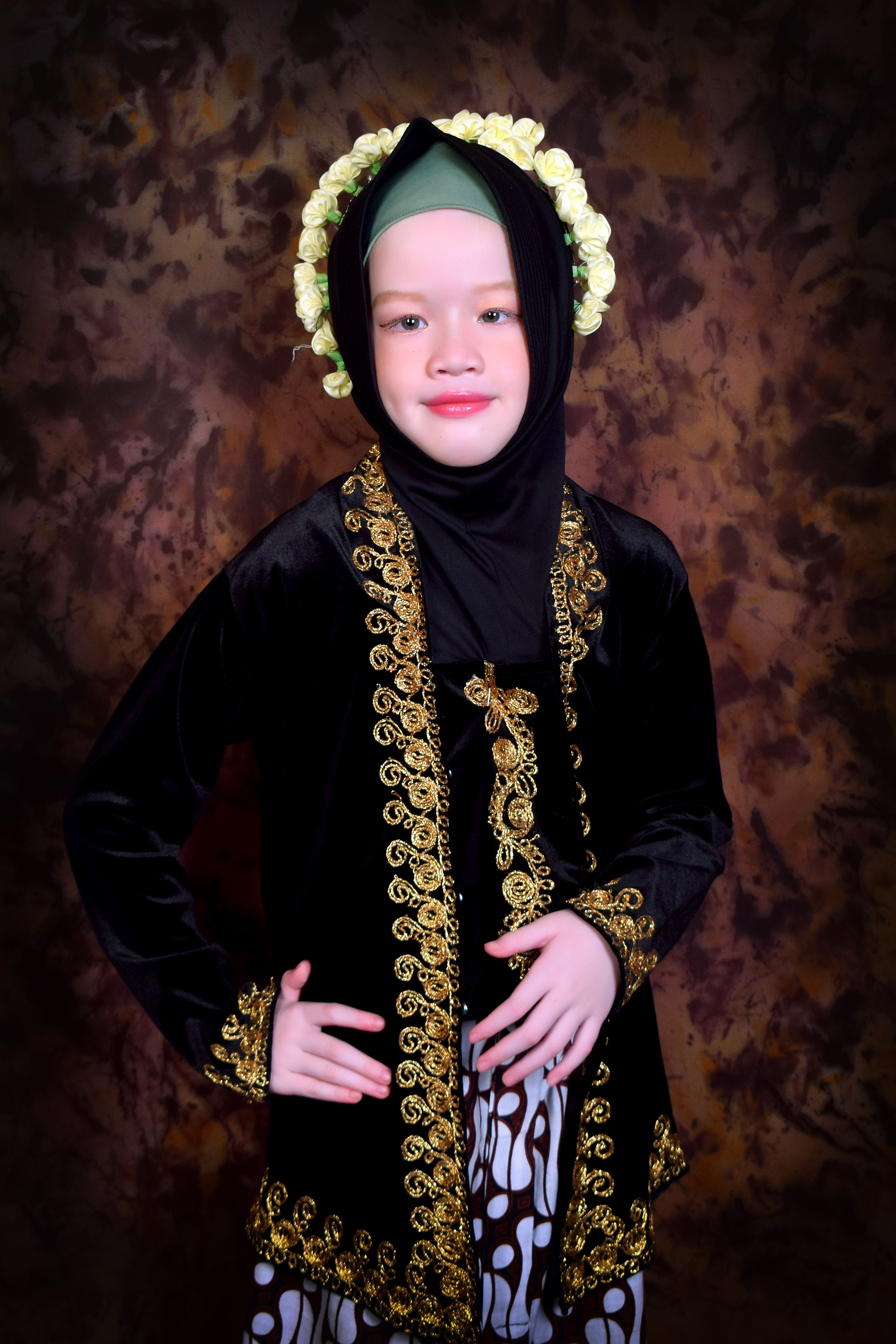Young girl in traditional attire with floral headdress against brown backdrop.