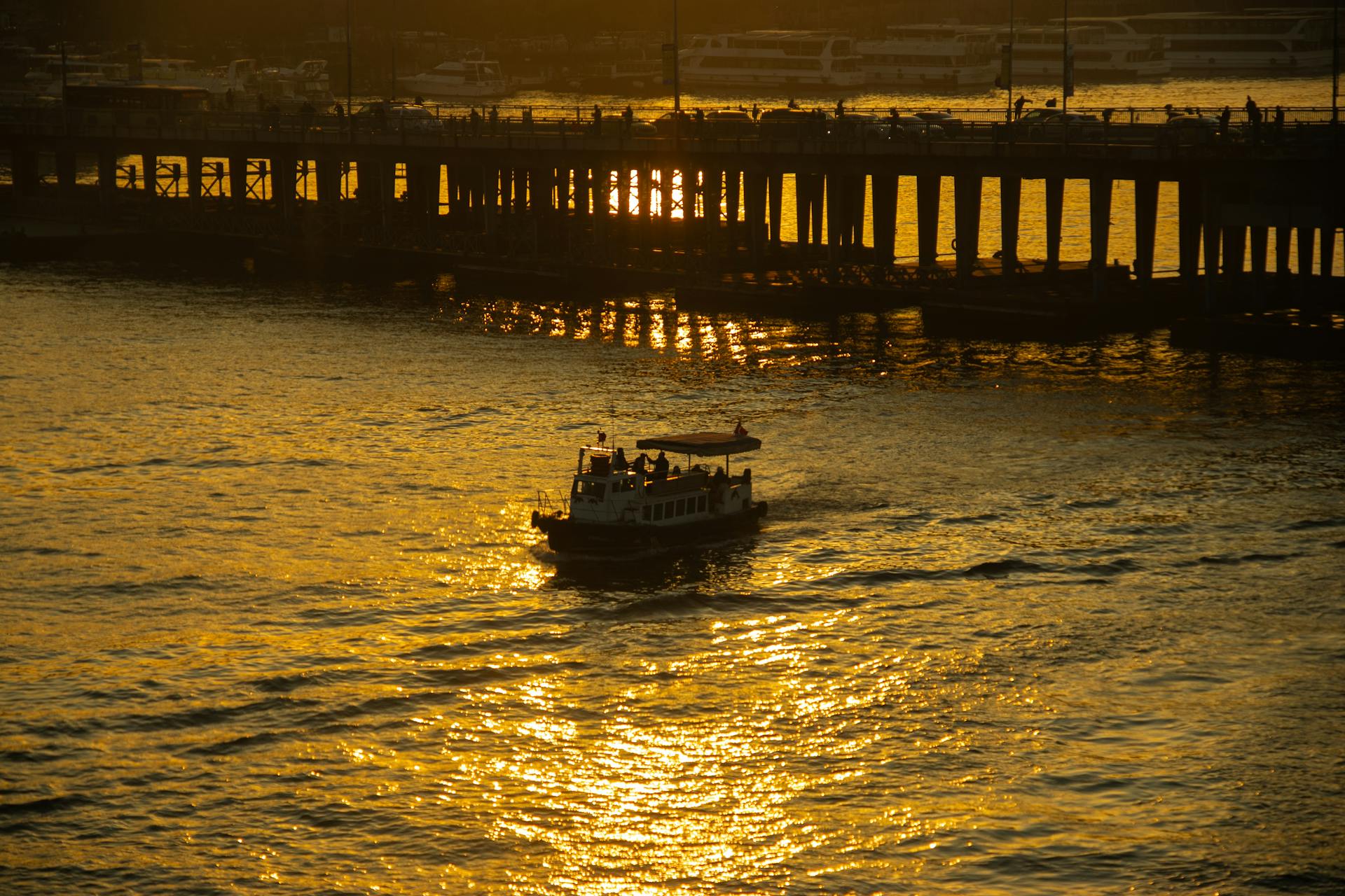 A scenic sunset view of İstanbul's Golden Horn with a boat and silhouette of a bridge.