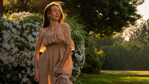 Free Woman in a flowing dress strolling through a garden during golden hour. Stock Photo