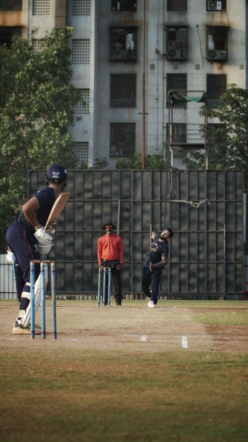 Free Cricket match action with bowler mid-delivery and batsman ready in urban Mumbai setting. Stock Photo