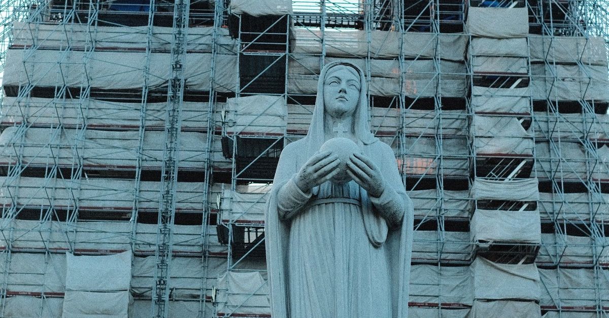 Photo by Tris Truong Statue of woman in prayer with scaffolding-covered historic building in background.