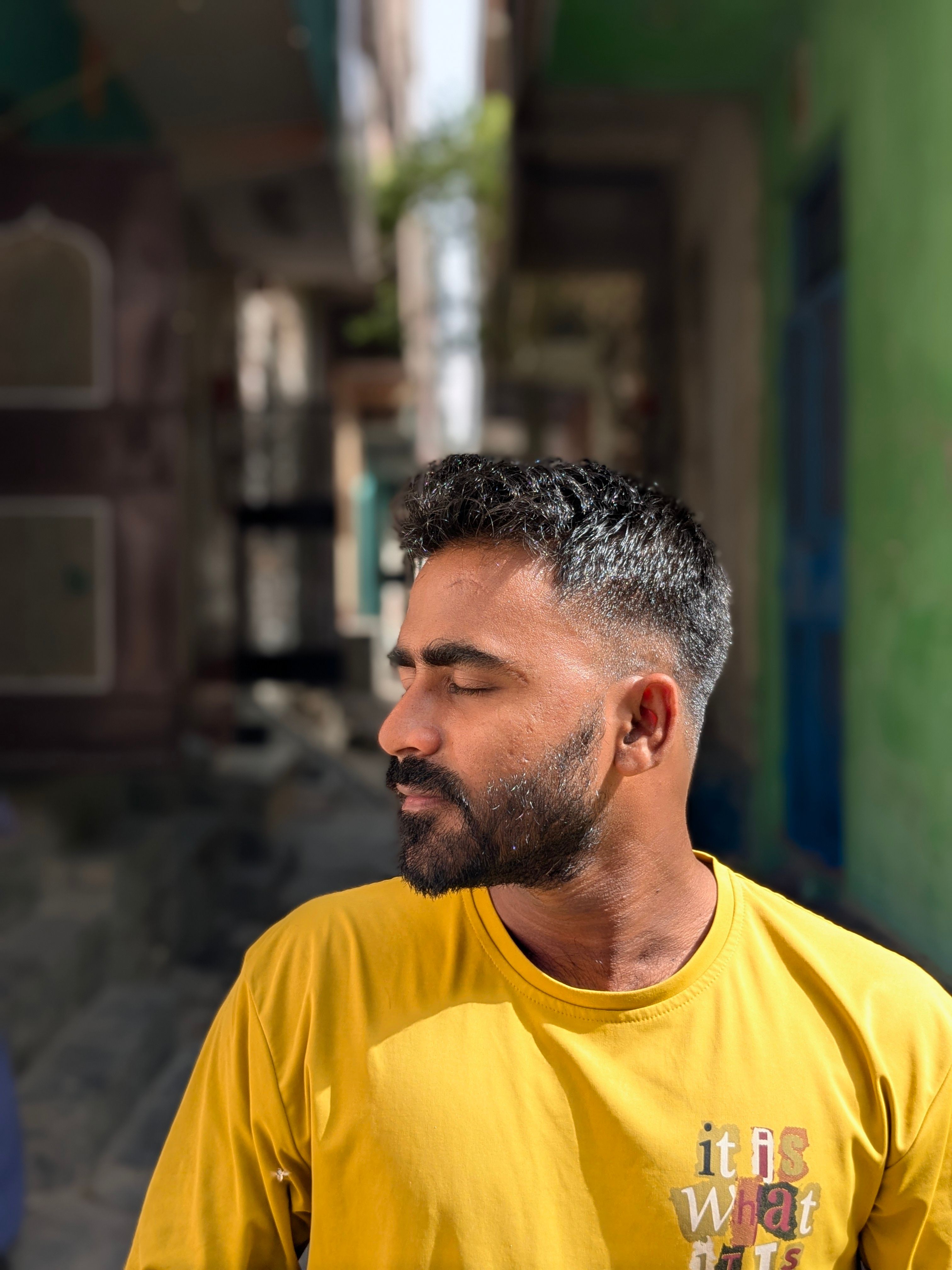 Side profile of a man enjoying the sun on a narrow street, wearing a yellow shirt.