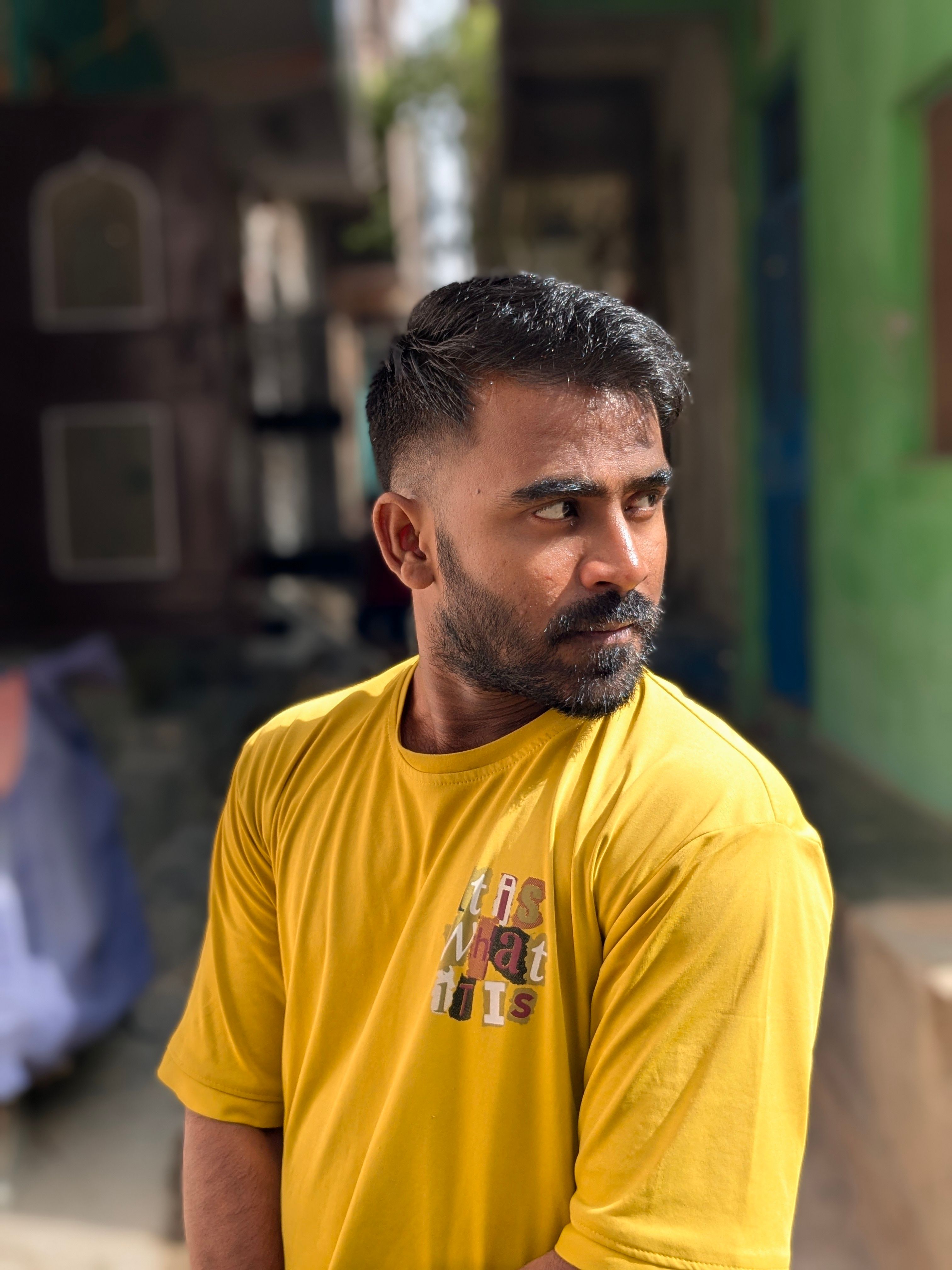 Portrait of a bearded man in a yellow shirt with a contemplative look, standing outdoors.