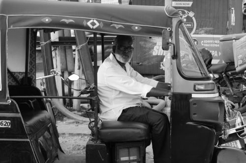 Free An elder man driving a traditional rickshaw in an urban setting, captured in black and white. Stock Photo