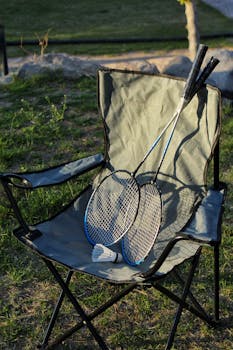 Two badminton rackets and a shuttlecock on a camping chair outdoors.