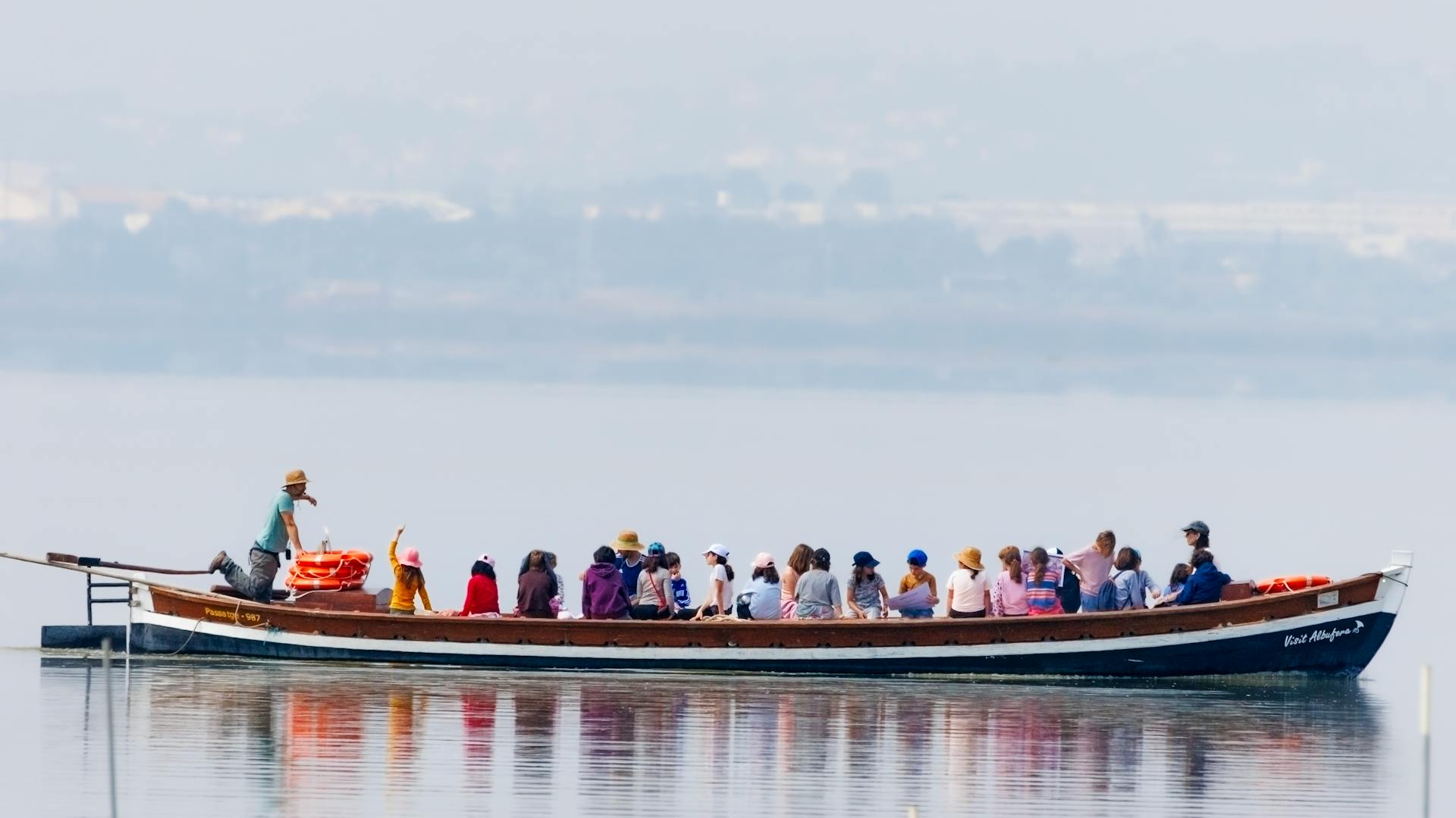 A diverse group enjoys a calm boat ride on a serene lake with scenic landscapes in the background.