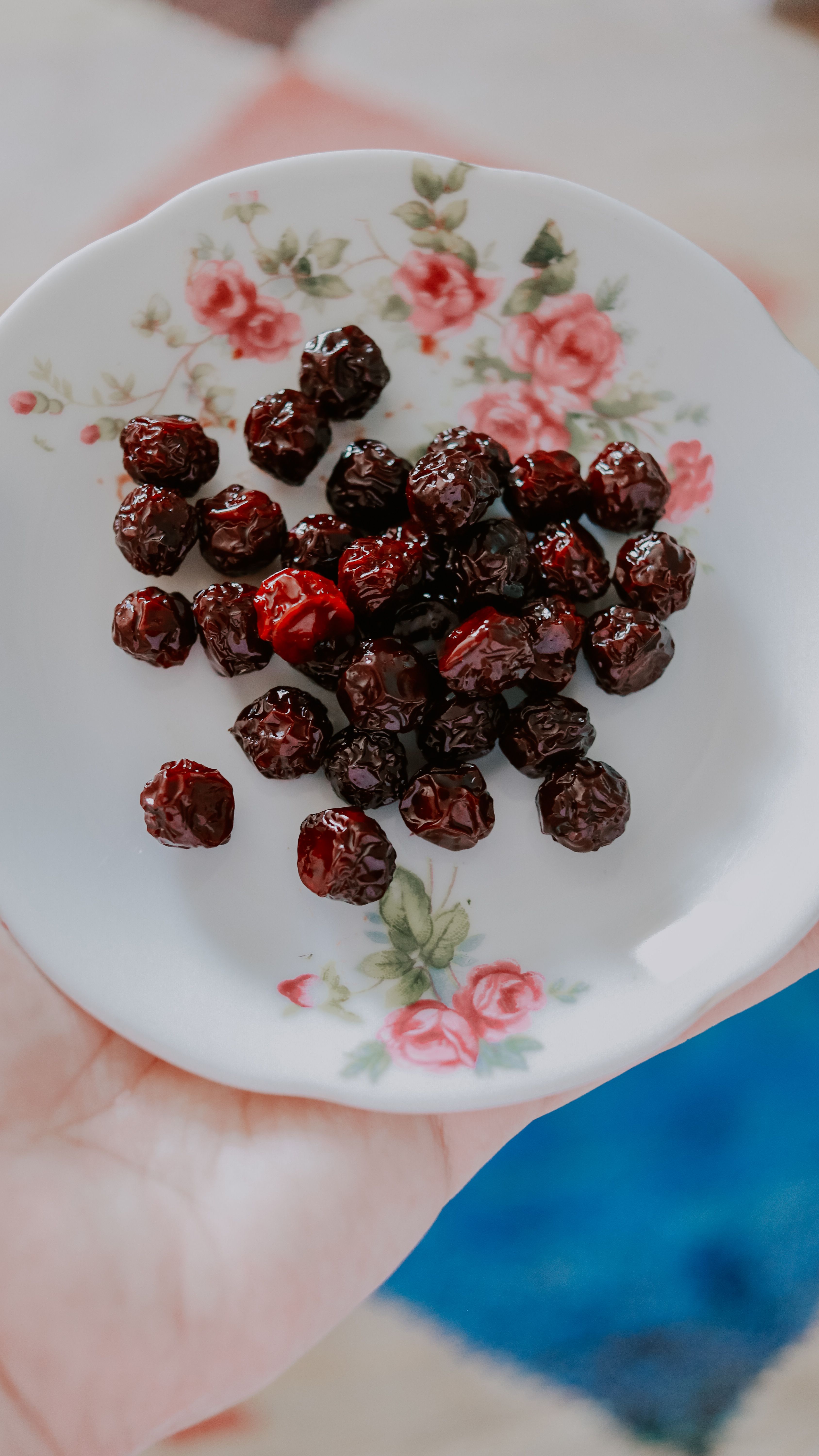 A hand holds a floral plate filled with dried cherries, showcasing a vibrant snack.