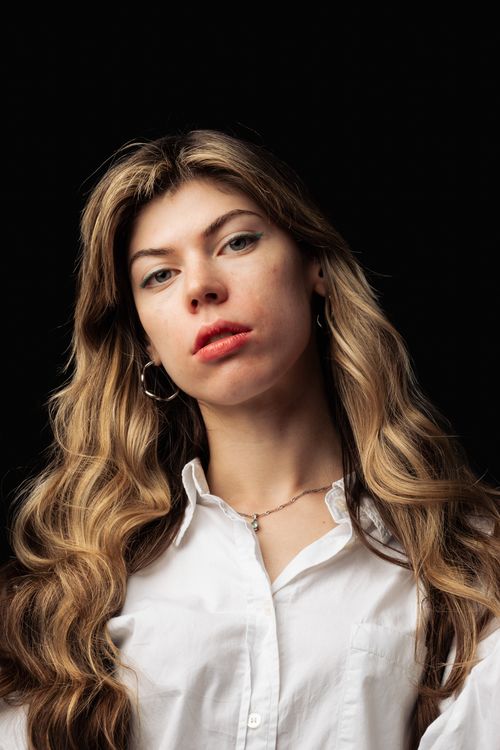 Free Close-up portrait of a woman with long blonde hair and white shirt against a dark background. Stock Photo
