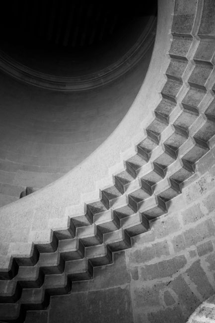 Black and white photo of a spiral stone staircase featuring geometric design in Pierrefonds, France.