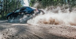 一辆汽车在尘土飞扬的森林道路上飞驰，扬起巨大的尘埃云