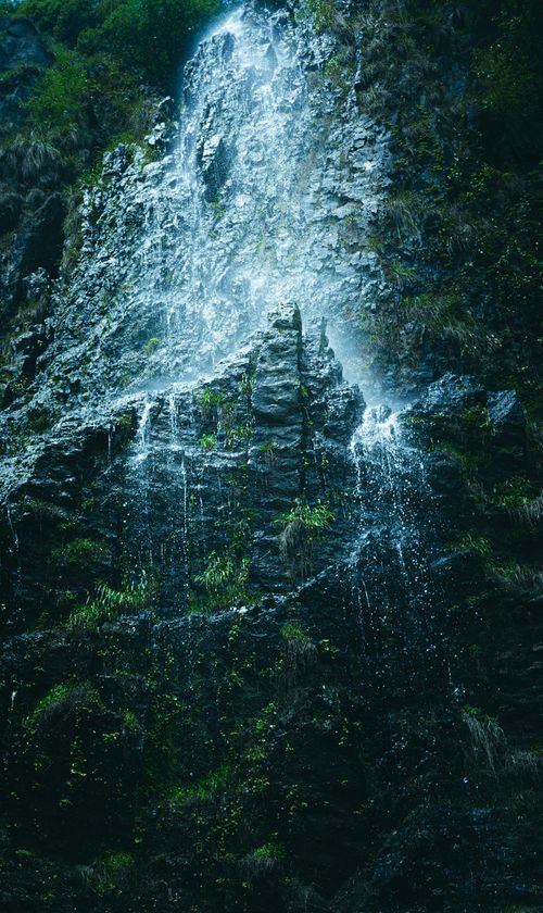 Free Tranquil waterfall cascading down a rocky cliff surrounded by lush greenery, creating a peaceful atmosphere. Stock Photo