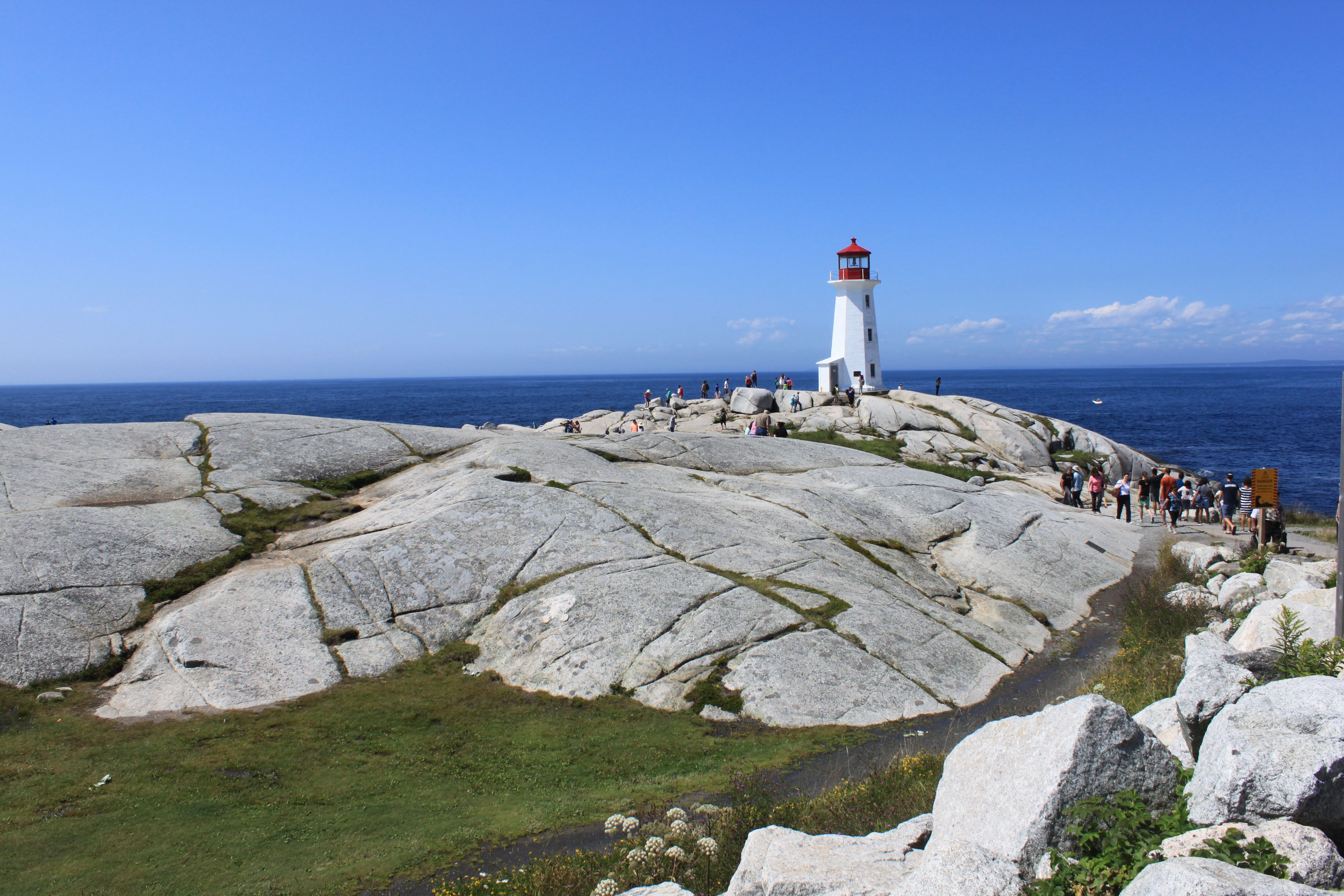 Scenic view of Peggy's Cove Lighthouse with tourists on a sunny day in Nova Scotia, Canada.