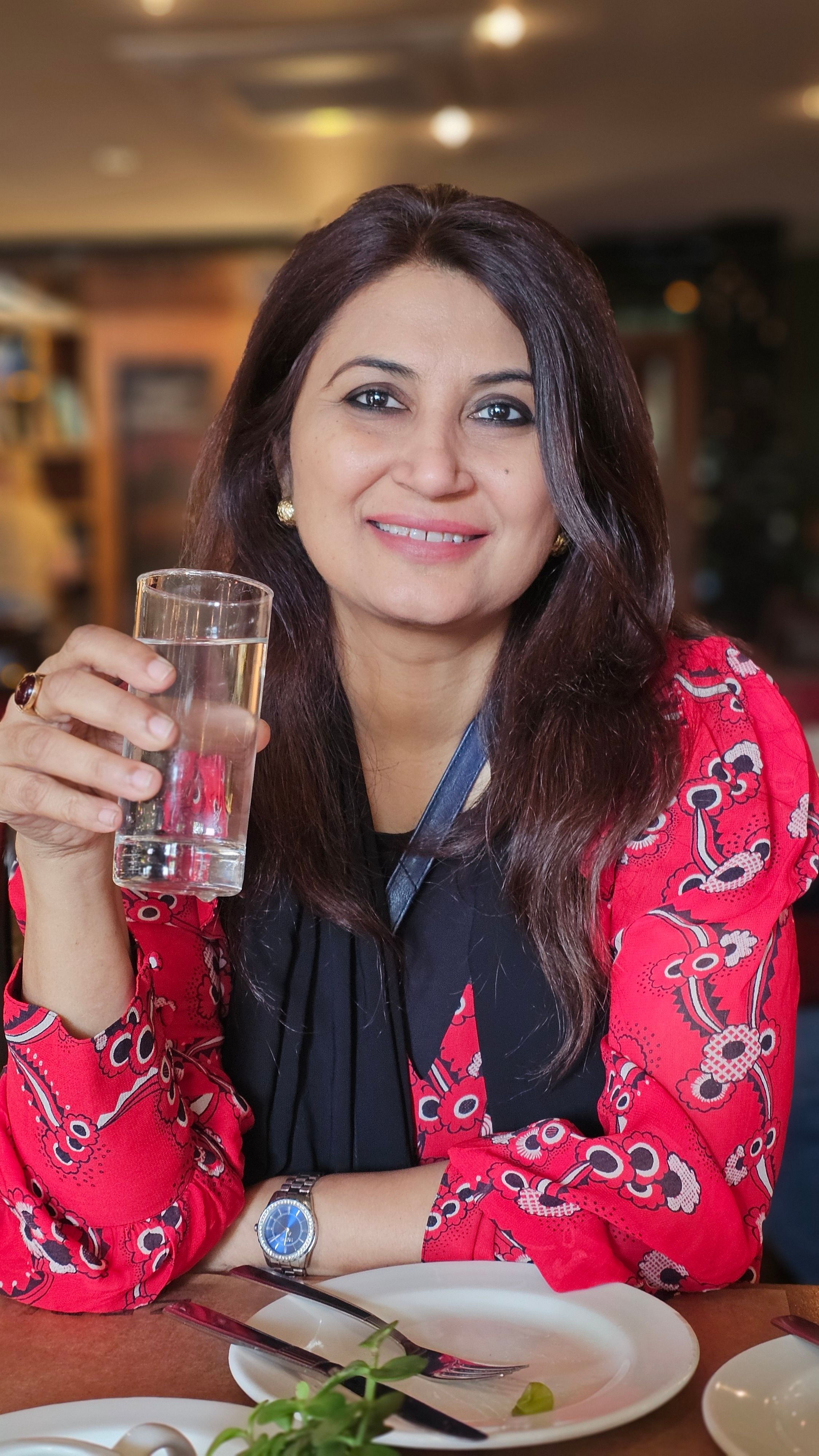 Woman in a colorful dress enjoys a refreshing glass of water indoors with a smile.