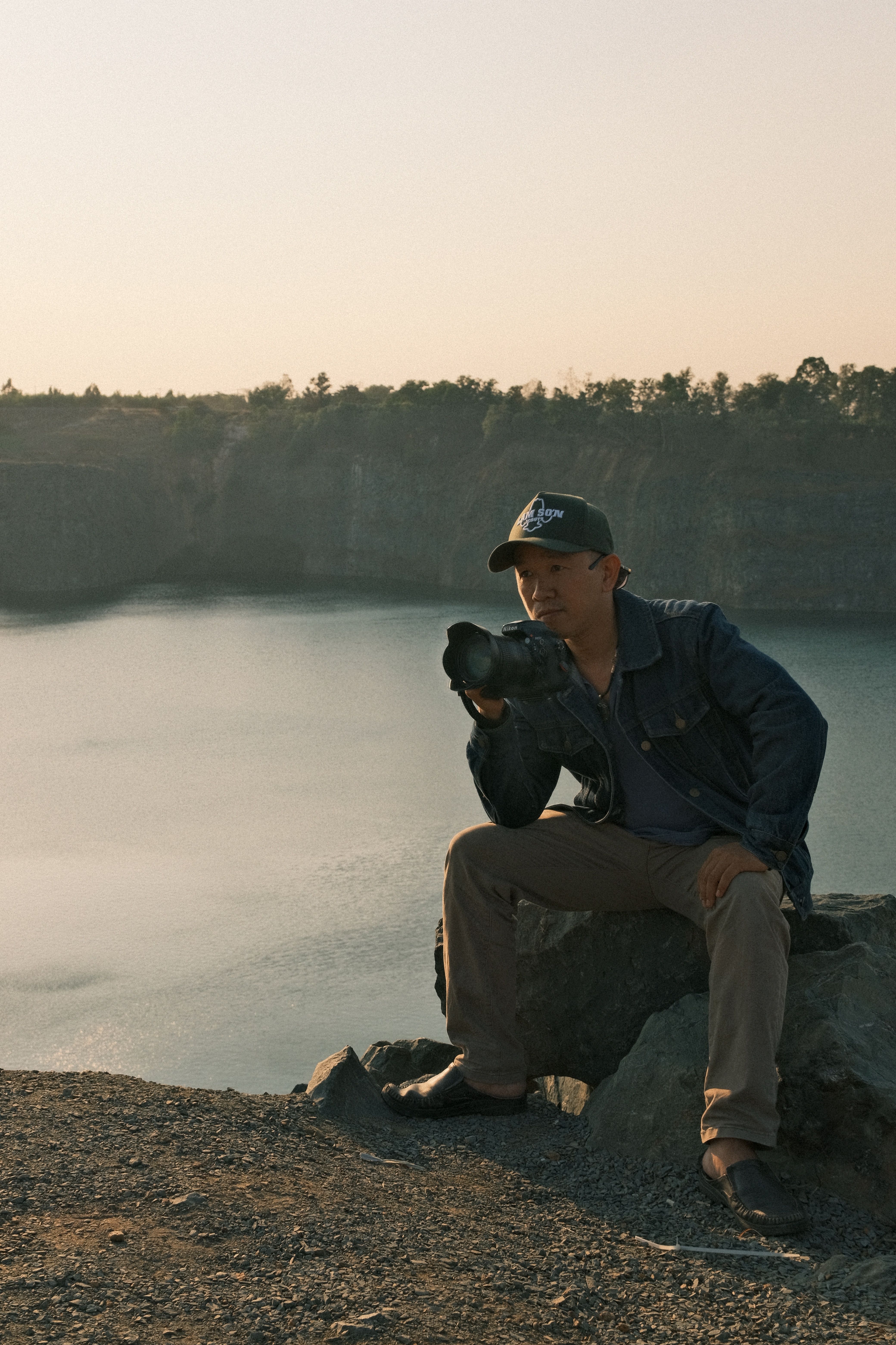 Man sitting by a lake taking photos at sunset, blending nature with photography.