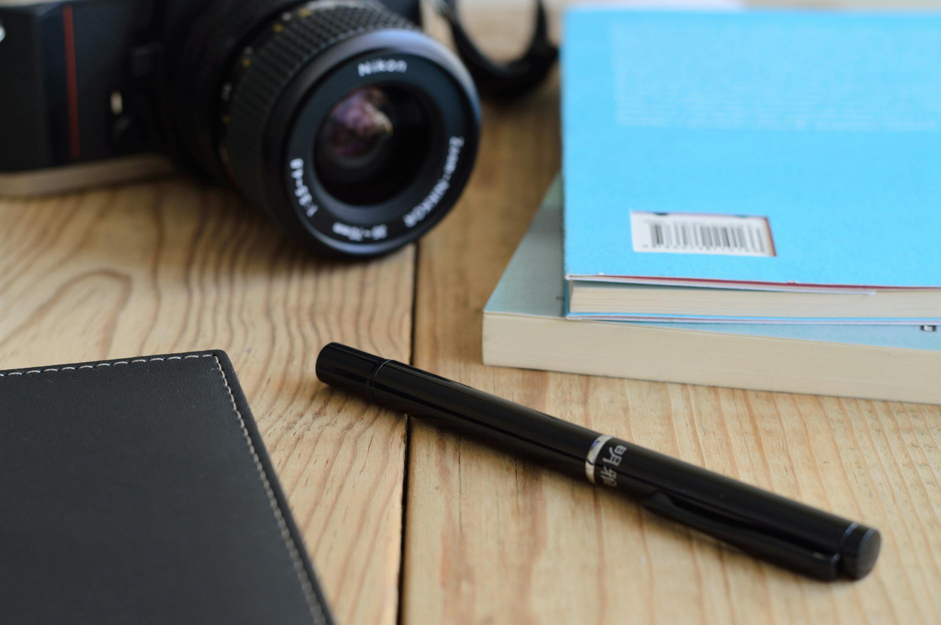 A close-up of a DSLR camera, books, and a pen on a wooden desk.