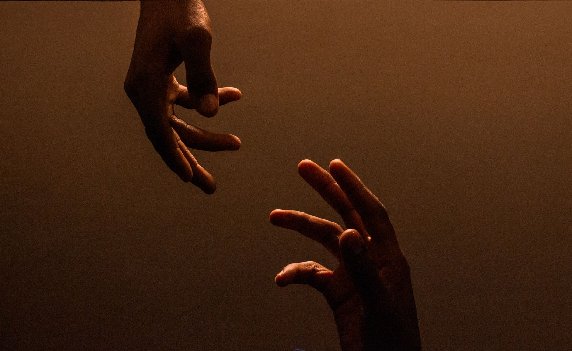 Two hands reaching towards each other against a dark, warm background, symbolizing connection.